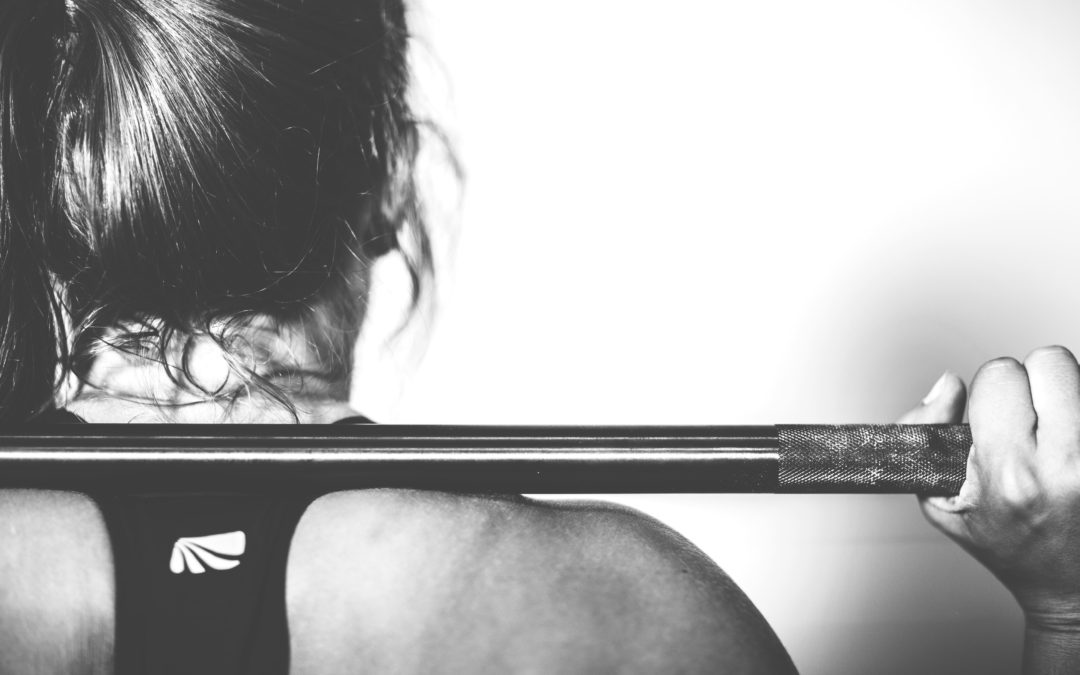 Athlete lifting a barbell behind her neck in a coached training session